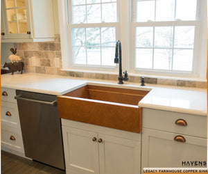 Large farmhouse sink with a brown copper patina and prominent apron front.